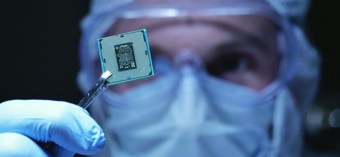 In Ultra Modern Electronic Manufacturing Factory Design Engineer in Sterile Coverall Holds Microchip with symbols in futuristic holography. Artificial intelligence